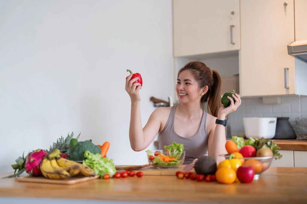 A joyful Jess Carter looking at a red and green bell pepper in her hands while developing a new recipe in her kitchen for CravyBite Kitchen.
