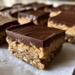 A close-up of a square peanut butter bars piece showing the thick peanut butter base and smooth chocolate topping.