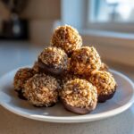 A stack of homemade pecan pie balls coated in chopped nuts and partially dipped in chocolate.