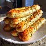 A tempting stack of soft, golden-brown garlic breadsticks topped with melted cheese and parsley, ready to eat.