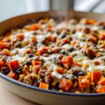 Close-up of a bubbling sweet potato skillet topped with melted cheese, ground meat, black beans, and corn.