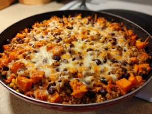 Close-up of a savory sweet potato skillet topped with melted cheese, ground meat, black beans, and corn.