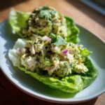 Two servings of creamy avocado chicken salad nestled in crisp lettuce cups, garnished with red onion and cilantro.