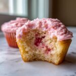 Close-up of a bitten strawberry cupcakes showing the moist cake and bright pink filling/frosting.
