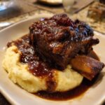 Close-up of a tender braised short ribs piece covered in rich, dark sauce, served over creamy mashed potatoes.