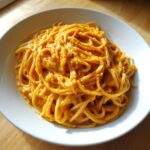 A close-up of spaghetti coated generously in a rich, orange butternut squash pasta sauce in a white bowl.