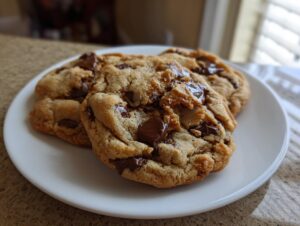 Close-up of three freshly baked, thick, and chewy chocolate chip cookies piled on a small white plate.
