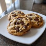 Three golden brown, thick, and chewy chocolate chip cookies loaded with melted chocolate chunks on a white square plate.