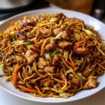 A close-up of a generous serving of homemade chicken chow mein recipe on a white plate.