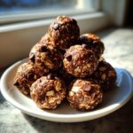 A close-up, sunlit stack of homemade chocolate chip protein balls made with oats, resting on a small white plate.