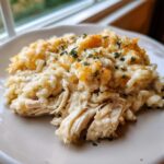 A close-up of creamy crock pot chicken and rice topped with melted cheddar cheese and parsley.