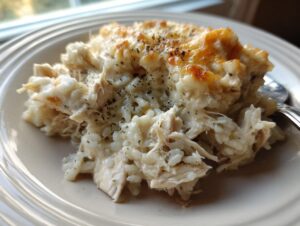 Close-up of a serving of creamy crock pot chicken and rice topped with melted, browned cheese and herbs.