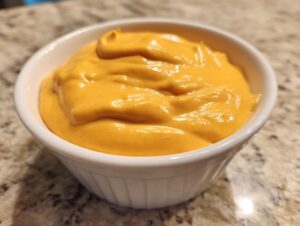 Close-up of thick, vibrant orange nacho cheese sauce swirled inside a small white ramekin.