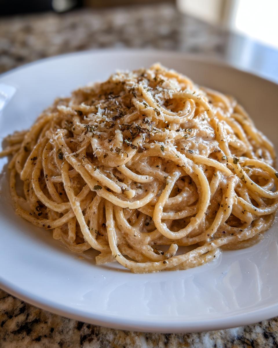 Close-up of creamy parmesan pasta tossed in sauce and topped with grated cheese and dried herbs.
