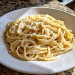 Close-up of creamy parmesan pasta tossed in sauce and topped with grated parmesan cheese and black pepper.
