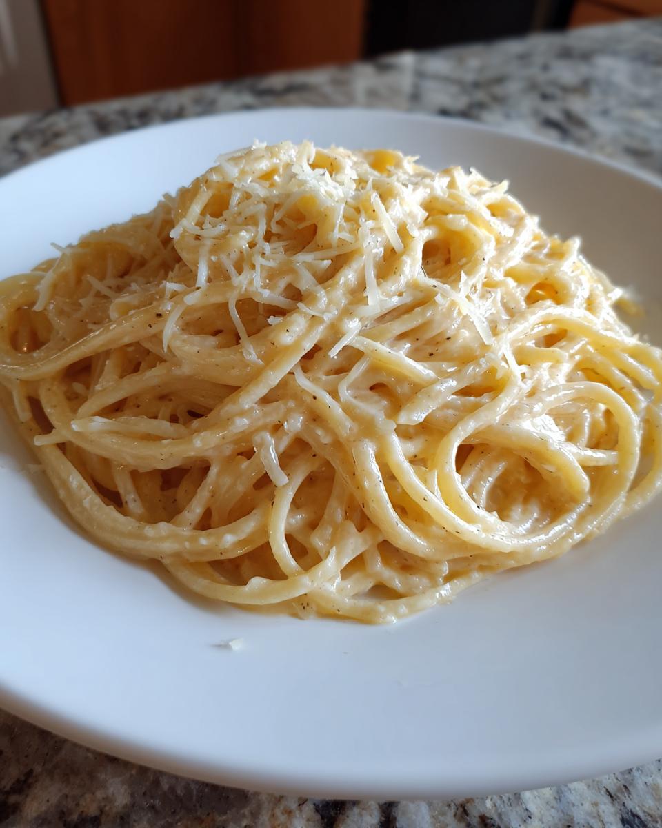 A close-up of a serving of creamy parmesan pasta, topped generously with freshly shredded parmesan cheese.