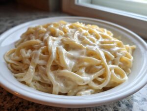 Close-up of fettuccine pasta generously coated in creamy Olive Garden Alfredo Sauce, served in a white bowl.