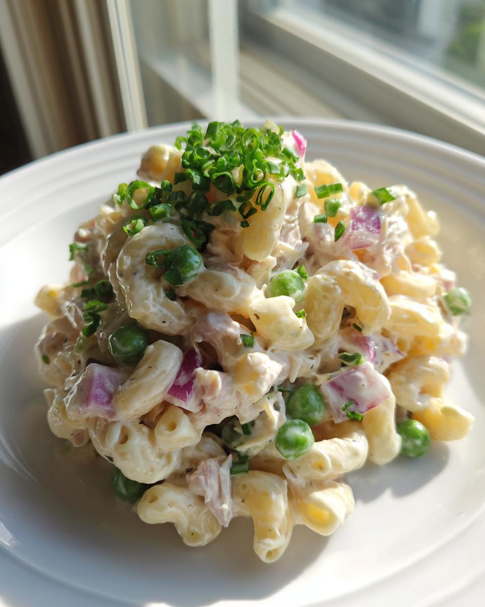A serving of creamy tuna pasta salad with elbow macaroni, peas, red onion, topped with fresh chives.