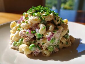 A mound of creamy tuna pasta salad featuring elbow macaroni, peas, red onion, and topped with fresh chives.