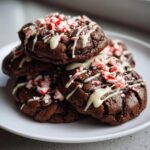 A stack of fudgy double chocolate peppermint cookies drizzled with white chocolate and topped with crushed candy canes.