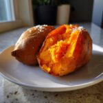 Two halves of a fluffy baked sweet potato sprinkled with coarse sea salt, showing bright orange flesh.