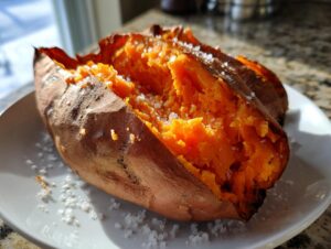 A close-up of a fluffy baked sweet potato, split open and sprinkled generously with coarse sea salt.