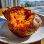 Close-up of fluffy baked sweet potatoes, split open to show the bright orange interior.