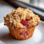 Close-up of a fluffy strawberry muffins with a golden brown streusel crumb topping and visible fresh strawberry pieces.