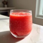 A vibrant, frozen strawberry daiquiri served in a clear glass sitting on a bright countertop.