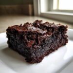 Close-up of a fudgy, dark chocolate sweet potato brownies slice topped with melted chocolate chips.