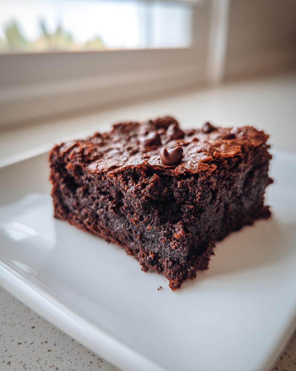 A close-up of a fudgy sweet potato brownies slice topped with melted chocolate chips on a white plate.