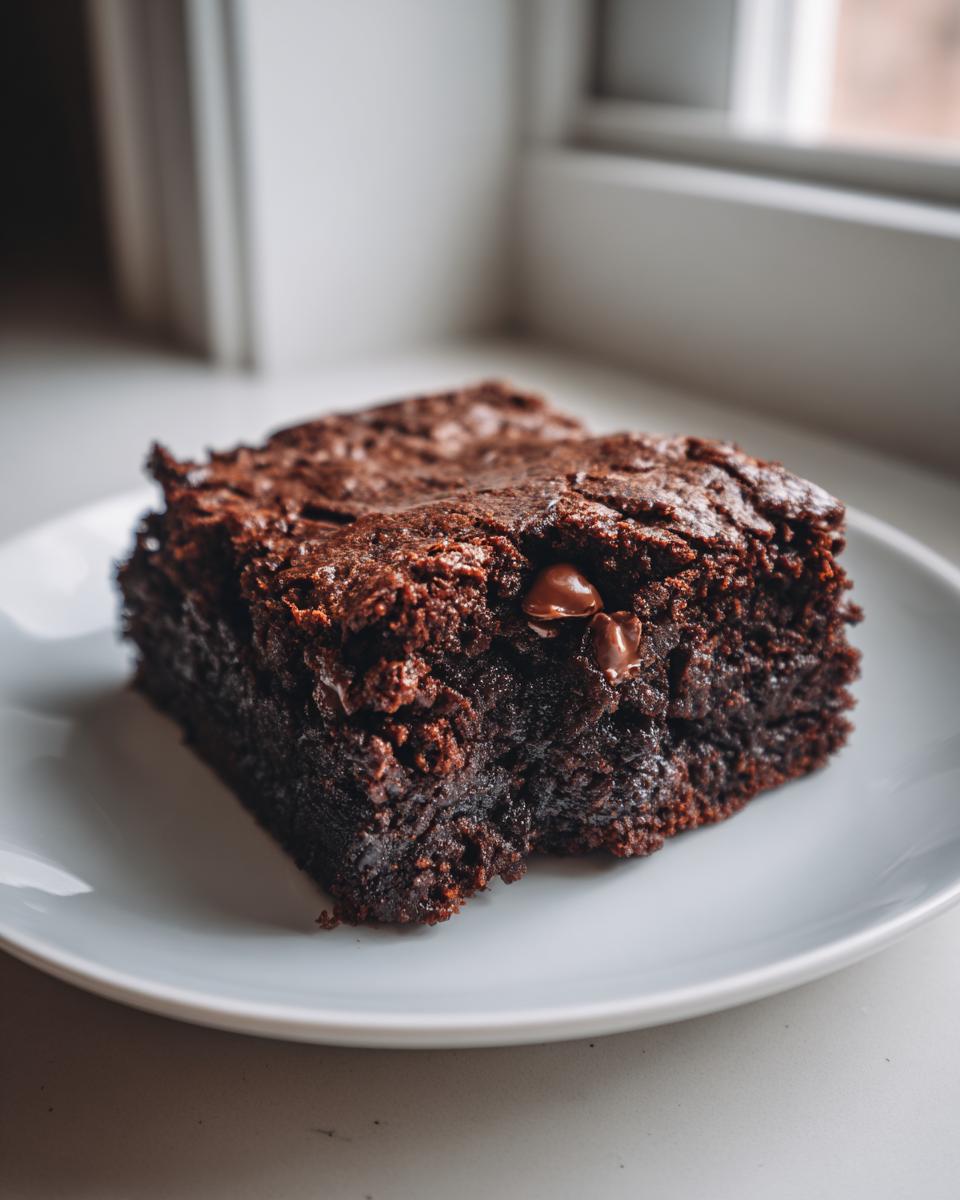 Close-up of a rich, fudgy square of sweet potato brownies with visible chocolate chips on a white plate.