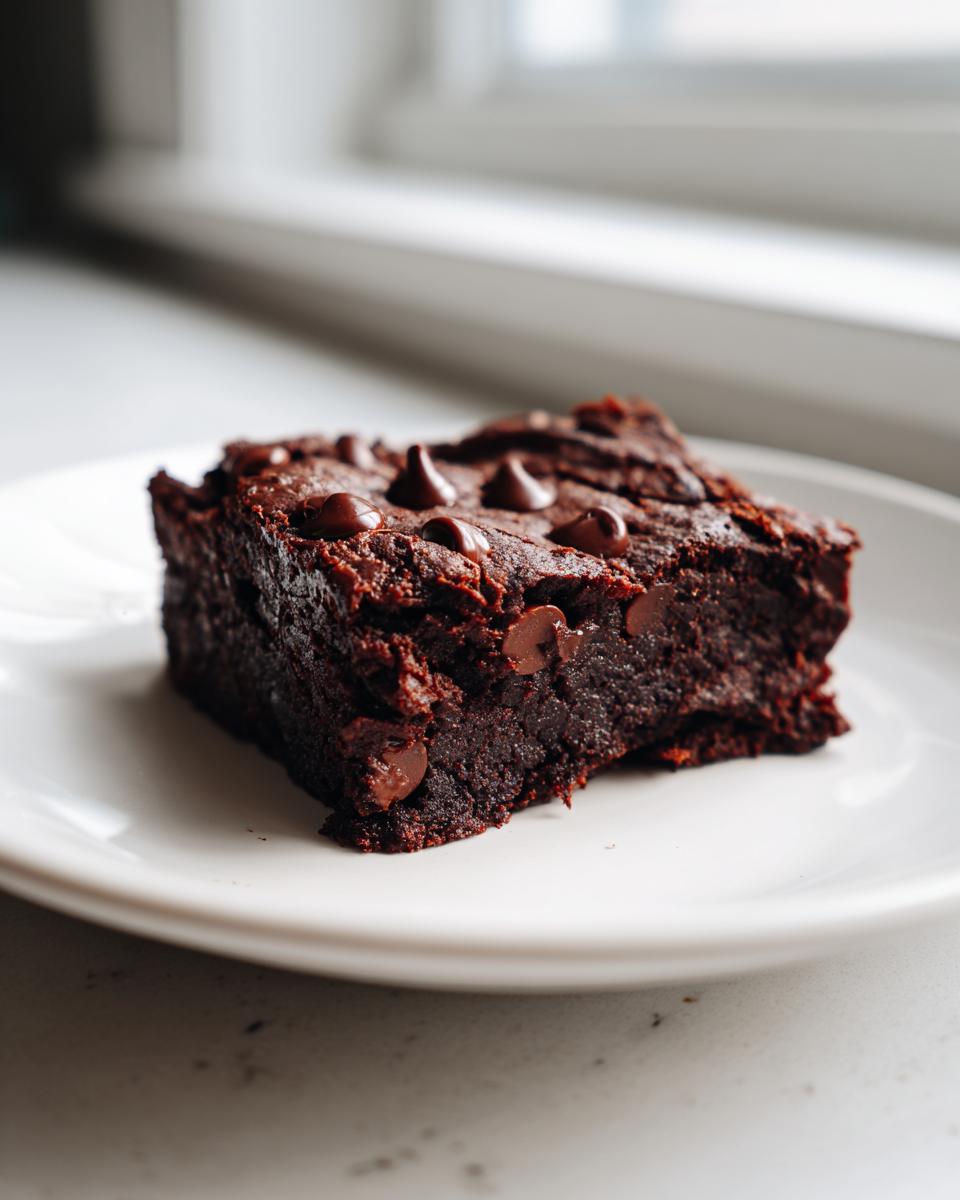 A single, fudgy square of sweet potato brownies topped with melted chocolate chips on a white plate.