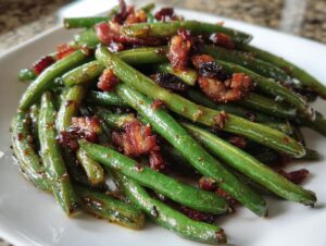 Close-up of glossy, bright green beans tossed in a honey garlic glaze and topped with crispy bacon pieces.