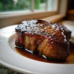 Close-up of a thick, juicy pork steak recipe cut, perfectly seared with a glossy glaze, resting in pan juices.