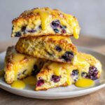 A stack of three delicious lemon blueberry scones drizzled heavily with bright yellow lemon glaze.