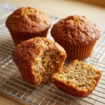 Close-up of moist bran muffins cooling on a wire rack, one muffin is broken open to show the texture.