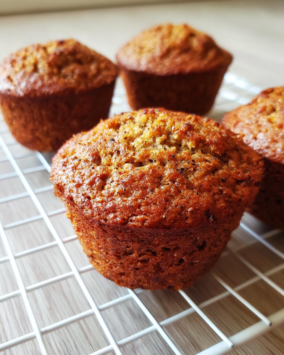 Close-up of four golden-brown bran muffins cooling on a white wire rack.