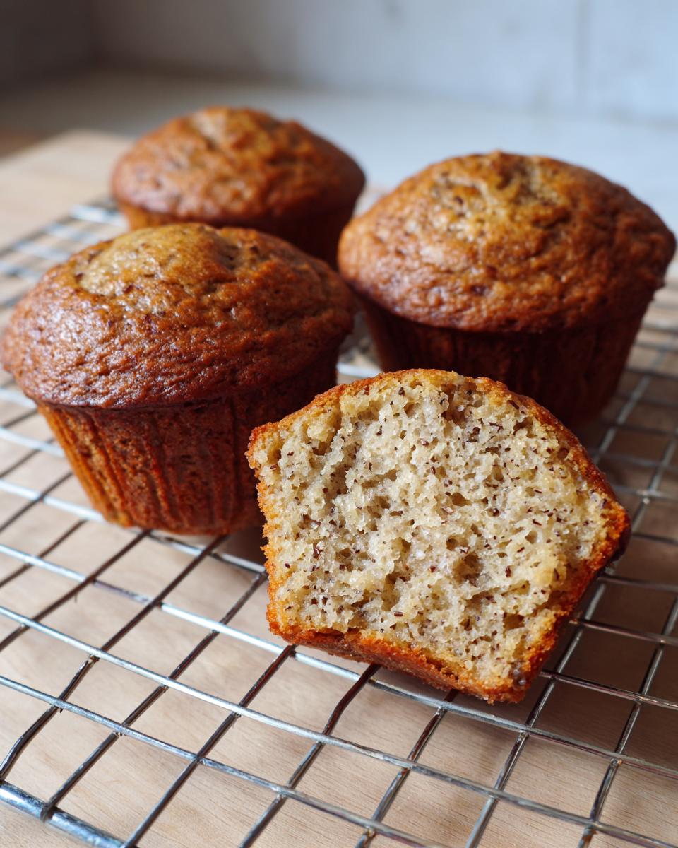 Close-up of moist bran muffins, one cut in half showing the texture, cooling on a wire rack.