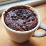 Close-up of a moist chocolate chip mug cake topped with melted chocolate chips inside a white mug.