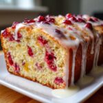 Close-up of a slice of moist cranberry orange cake drizzled generously with white citrus glaze.