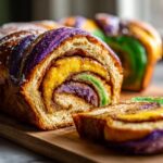Close-up of a moist King Cake loaf, sliced to show cinnamon swirl filling and vibrant purple, gold, and green sugar topping.