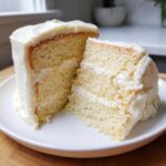 Close-up of a moist slice of vanilla cake recipe with thick white buttercream frosting.