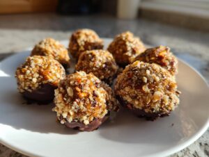 A plate of homemade pecan pie balls coated in chopped nuts and partially dipped in dark chocolate.