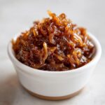 Close-up of deeply browned, glossy caramelized onions piled high in a small white bowl.
