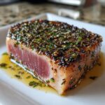 Close-up of a perfectly seared tuna steak, rare in the center, coated in a dark sesame and herb crust.