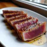 Five perfectly seared and sliced tuna steak pieces, showing a rare pink center, seasoned with a spice rub and sitting in a light marinade.