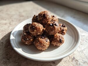 A stack of homemade protein balls made with oats and topped with mini chocolate chips, sitting on a light plate.