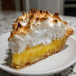 Close-up of a perfect slice of lemon meringue pie showing bright yellow filling and tall, toasted meringue peaks.