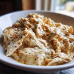 Shredded slow cooker garlic parmesan chicken coated in a rich, creamy, seasoned sauce, served in a white bowl.